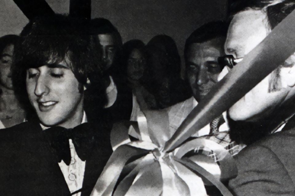 Black and white image of a man wearing a suit and cutting a ribbon. 