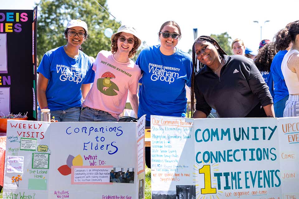 Students stand smiling behind signs with information about their community service groups.