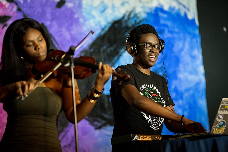 A person playing a violin and a person at a computer, on stage at Culture X