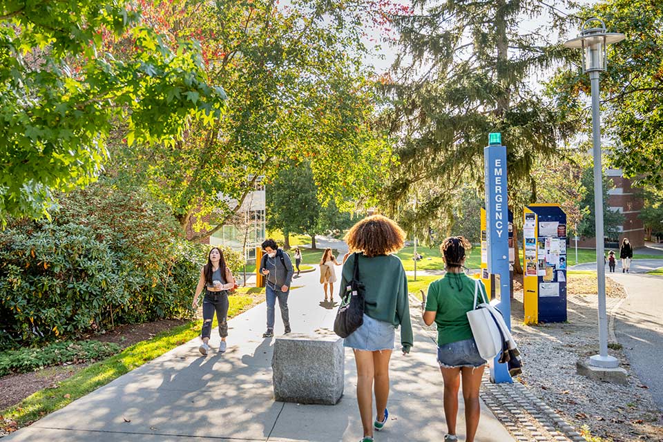 Masked students walking on campus, blue emergency light box in the foreground