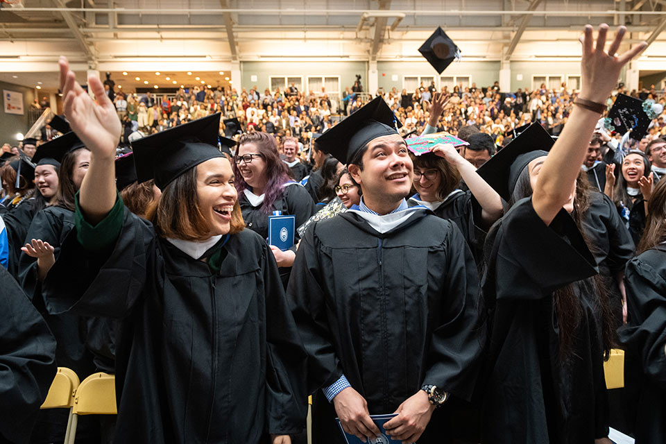 Students at Commencement smiling as mortarboards are thrown in the air