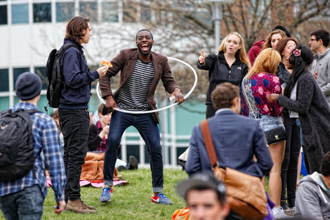 A young man holding a hoola hoop in a group of other young people smiles widely.