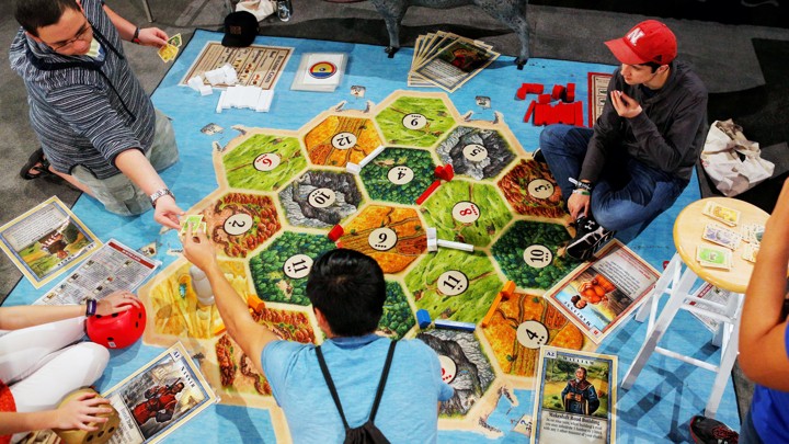 A group of young adults play the board game Catan.