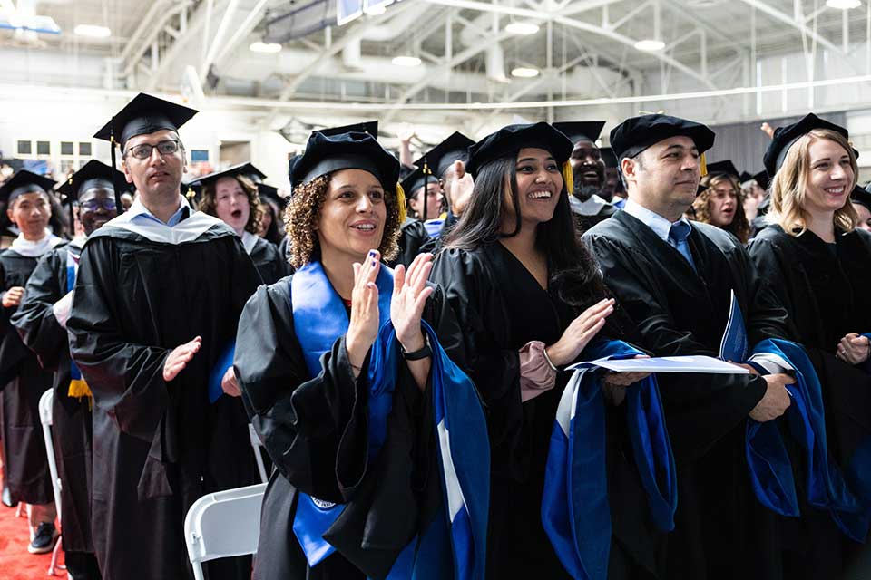 Students in caps and gowns clap during the Graduate Commencement Ceremony
