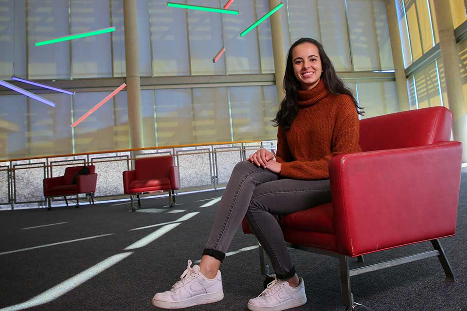 Cano sitting in a red chair in a room with colored lights hanging from the ceiling