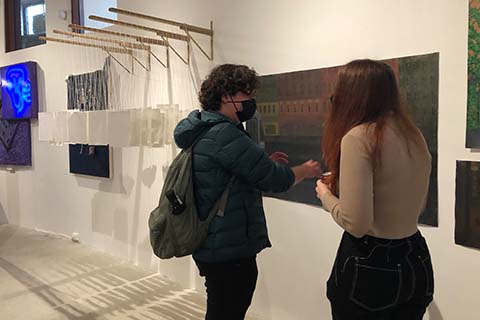 two students talking in front of Winter's artwork on the wall