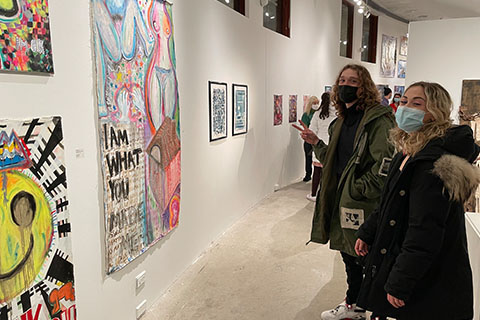 Audrey Rogers and a student standing in front of Roger's piece. The piece says "I am what you made me" in the bottom left, has women's bodies on the top, and a house and ear in the bottom right.