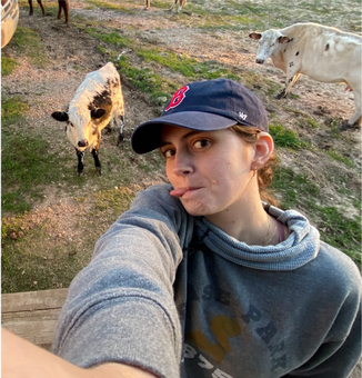 paige next to two cows and wearing a baseball cap