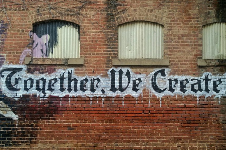 Brick wall with spray painted words: "Together We Create"