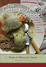 Book Cover. Text reads: The German-Jewish Cookbook. Gabrielle Rossmer Gropman and Sonya Gropman.  Recipes & History of a Cuisine. Foreword by Nach Waxman. Background photograph is a plage with stuffed cabbage and a fork and knife.  There is a white napkin with red stripes behind the plate.