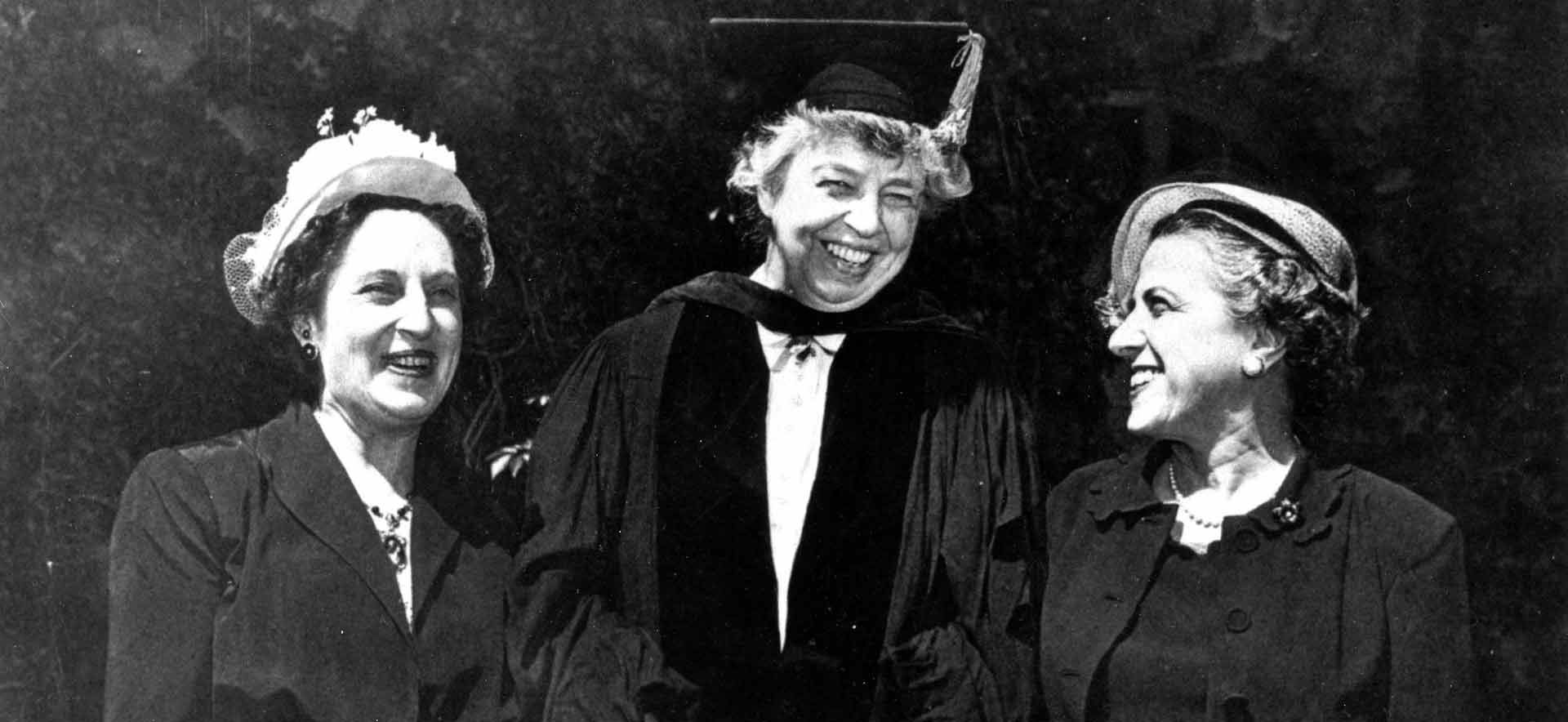 Eleanor Roosevelt wears a cap and gown and stands smiling between two other women.