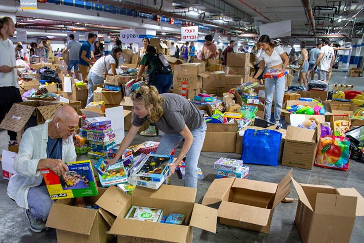 Group of people packing clothes and various items into boxes in a warehouse.