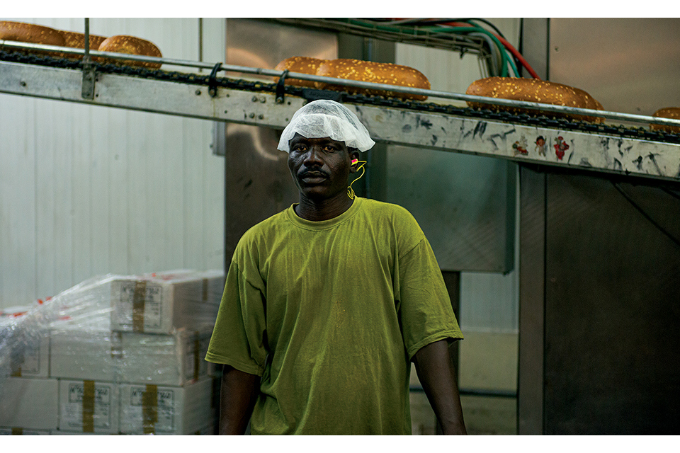Man standing in front of a conveyer belt full of loaves of bread