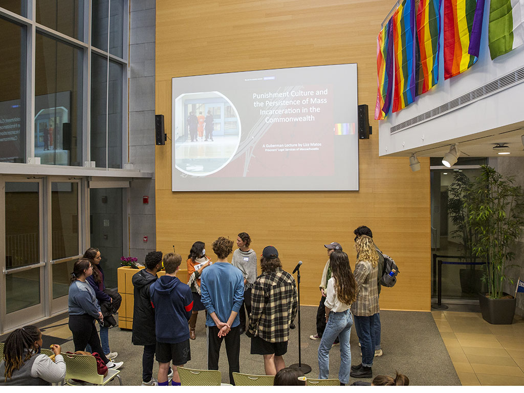 Elizabeth Matos and Rosalind Kabrhel speak with a group of Brandeis Students before the 2022 Guberman Lecture. Smart board on the wall behind the group shows the introductory slide titled: Punishment Culture and the Persistence of Mass Incarceration in the Commonwealth: A Guberman Lecture by Lizz Matos, Prisoners' Legal Services of Massachusetts.