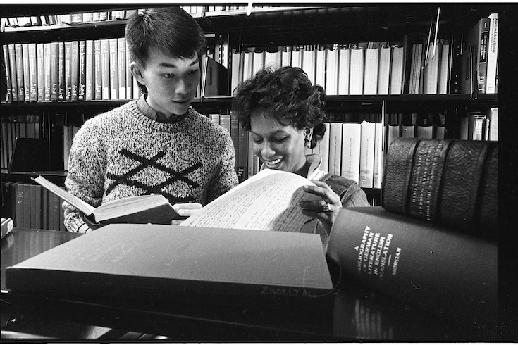 Archival photo of two people in the library stacks looking at open books.