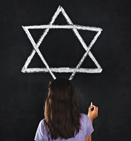 Photo of a little girl drawing a Star of David with chalk on a blackboard.