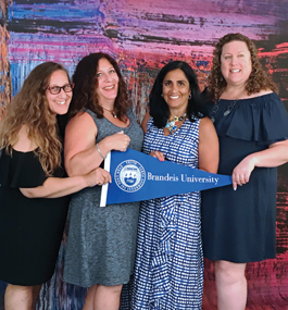 Four alumnae pose with a Brandeis banner.
