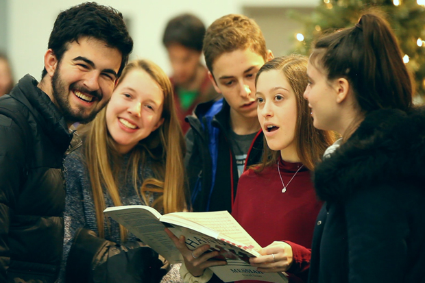 Students gathered around a songbook, smiling and singing