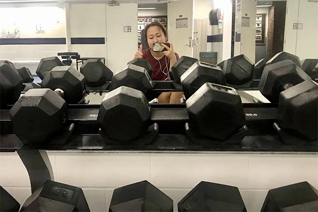 A student at a gym standing in front of a rack of weights