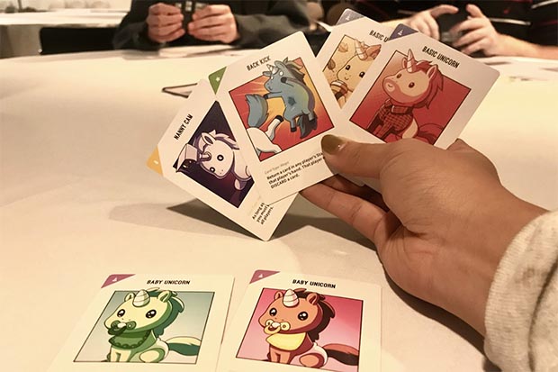 A student holds 4 cards from the Unstable Unicorn game. 
