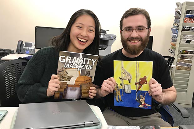 2 students hold past editions of the Gravity magazine.