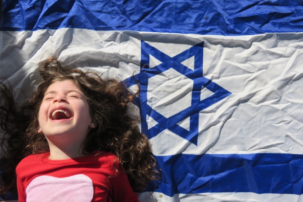 A little girl laughs in front of an Israeli flag