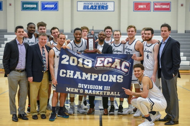 The Brandeis Judges basketball team, 2019 ECAC Division III champions with championship banner