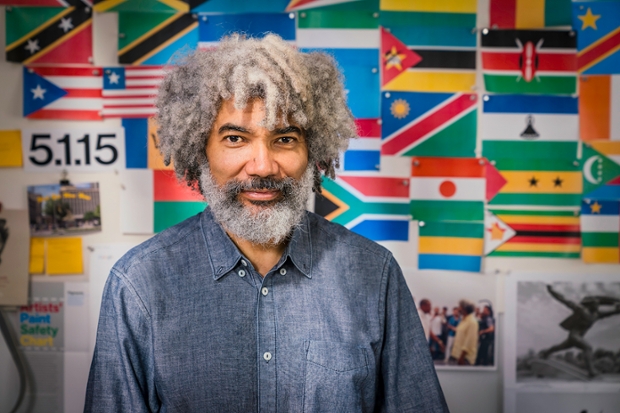 Artist Fred Wilson in front of a wall of flags and photographs