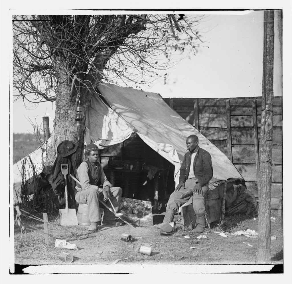 two former slaves sit in front of a tent next to a tree