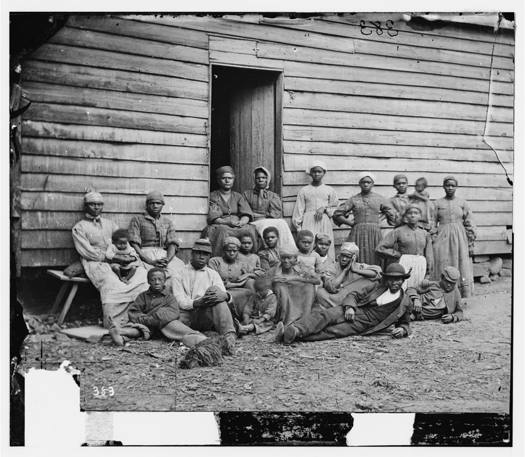  A group of escaped enslaved people in front of a clapboard refugee house in Virginia