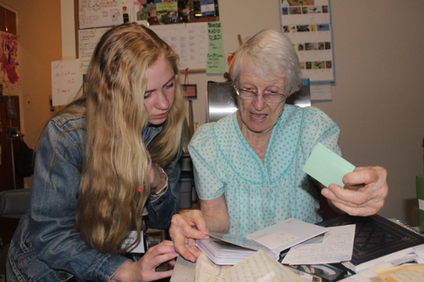 female student with long blond hair and denim jacket looks at letters with elderly woman in nightgown
