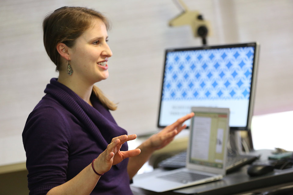 A psychology student teaching at the front of a class, pointing upward to a projection screen