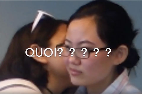 A student kisses another on the cheek with the word QUOI??? on the screen