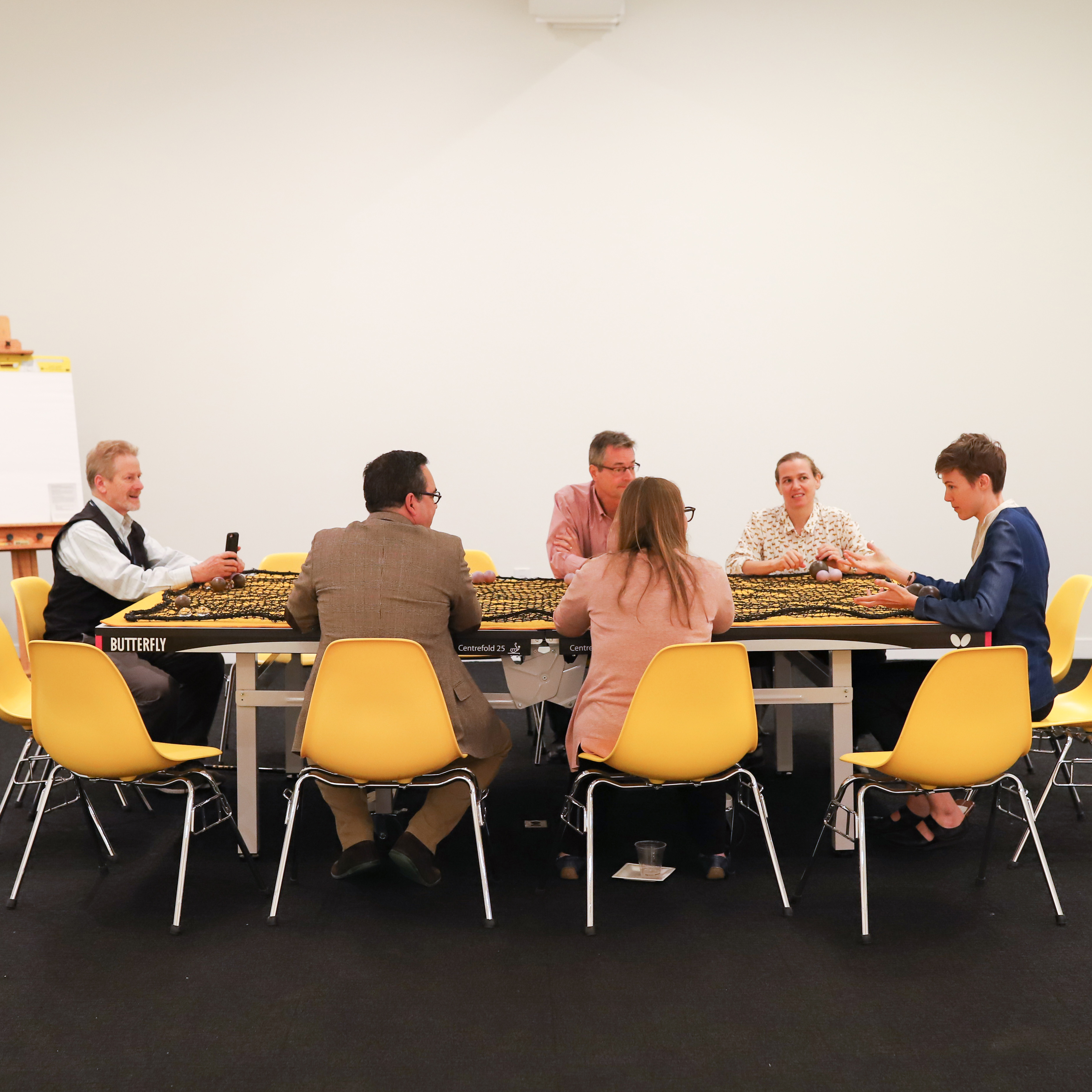 People sitting at a table in yellow chairs reading to engage with The Meeting Game