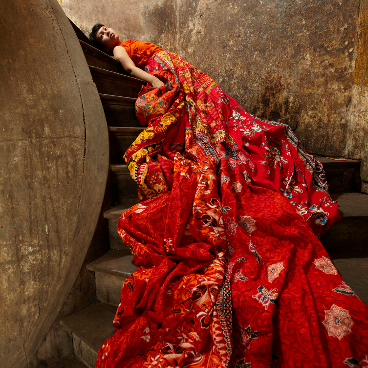 Artist Anida Ali in a red dress laying on stairs.