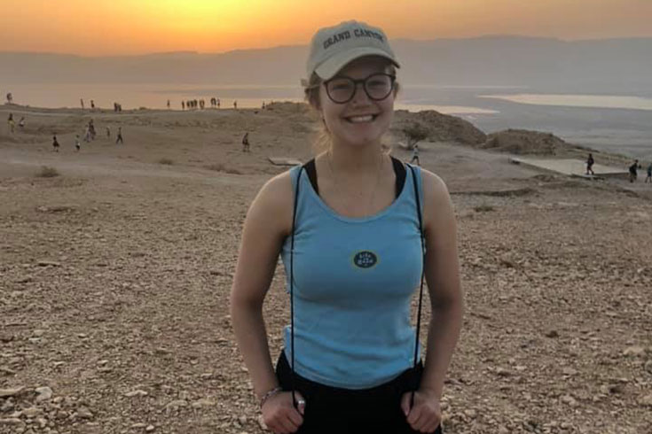 Natalie Fenwick standing in a desert in Israel, with the sun setting behind her