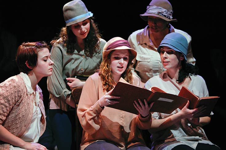 Women wearing hats gathered around an open book