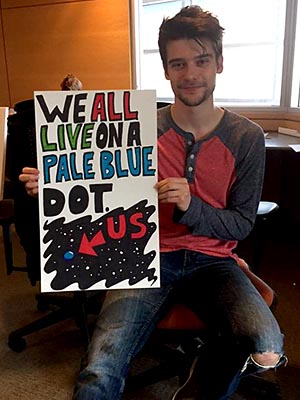 Student holding his poster which says: We all live on a pale blue dot