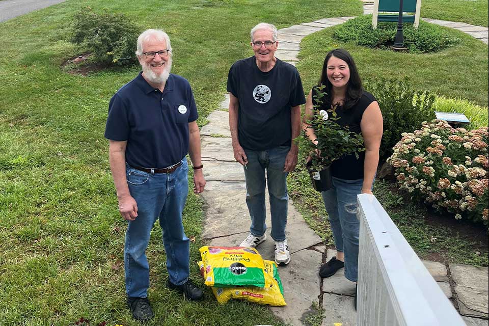 Three volunteers smile in front of a garden that they are planting