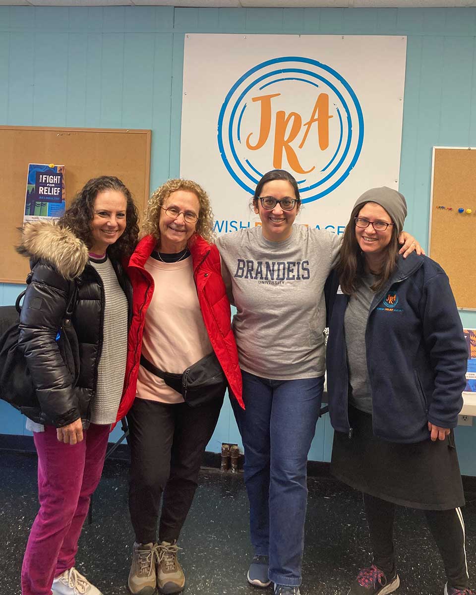 Four people stand smiling in front of the Jewish Relief Group sign