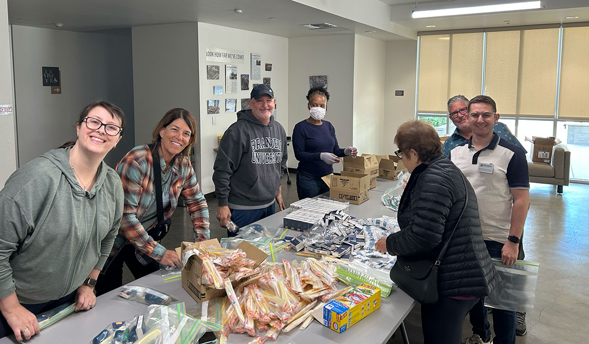 A group of volunteers stands around a table sorting various essential items into bags to be donated