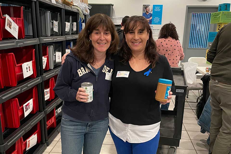 Two volunteers smile and hold canned food at The Ark.