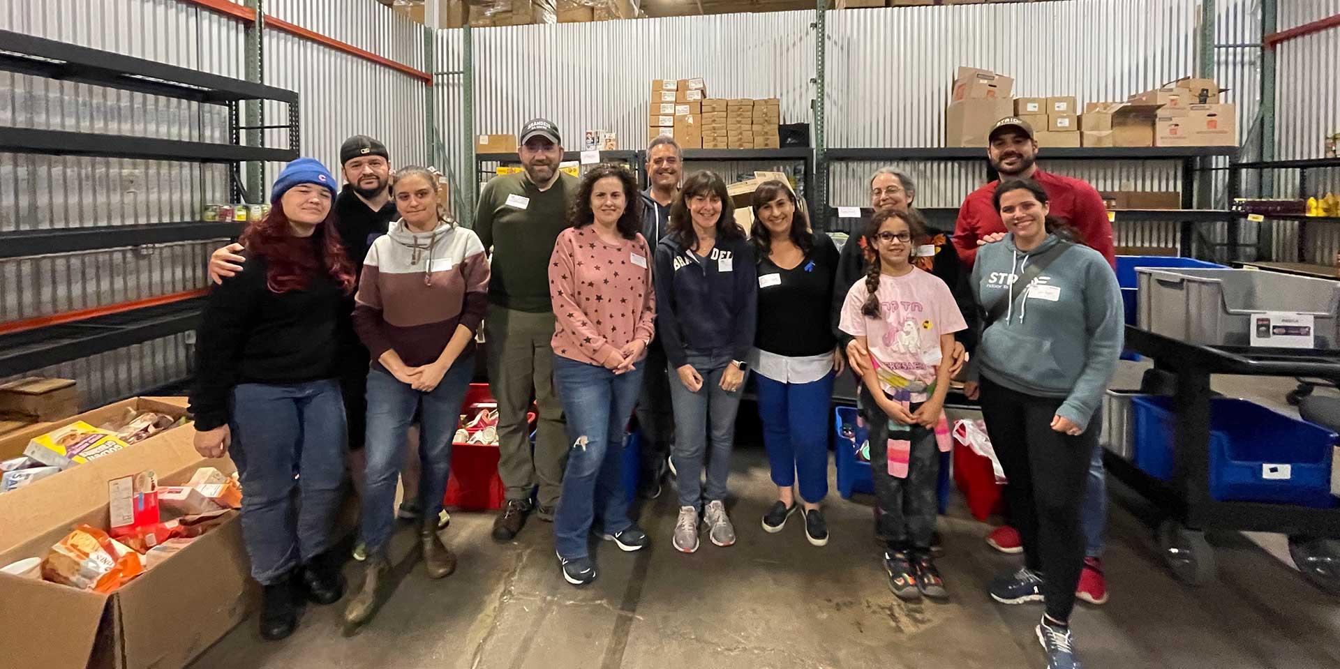 Group of volunteer Brandeis alumni and their families standing in the storage room of The Ark