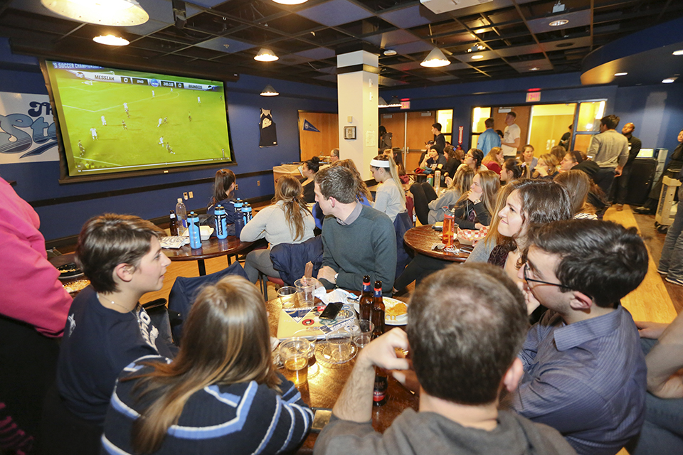 Students watching a soccer game on TV while eating and drinking. 