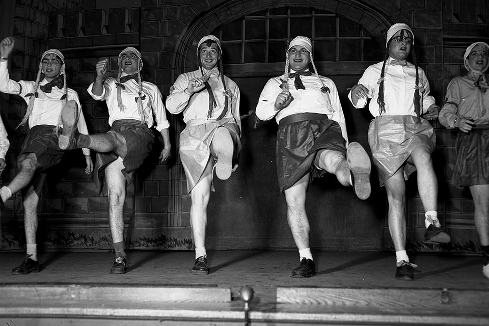 A group of students wearing costumes dance in a line.