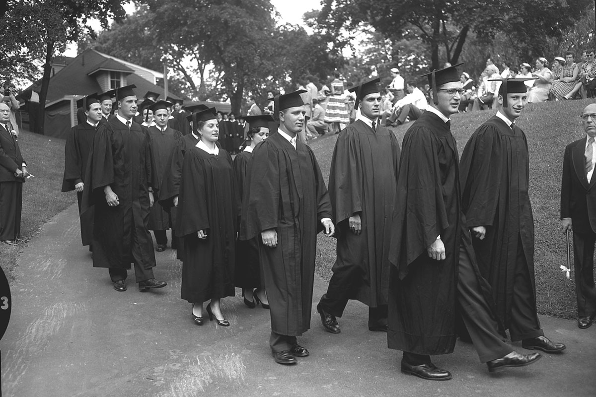 Students wearing caps and gowns walk in a graduation ceremony.