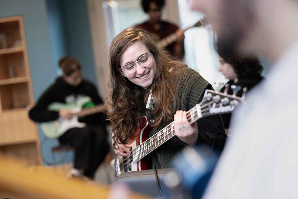 A student smiles while playing guitar.