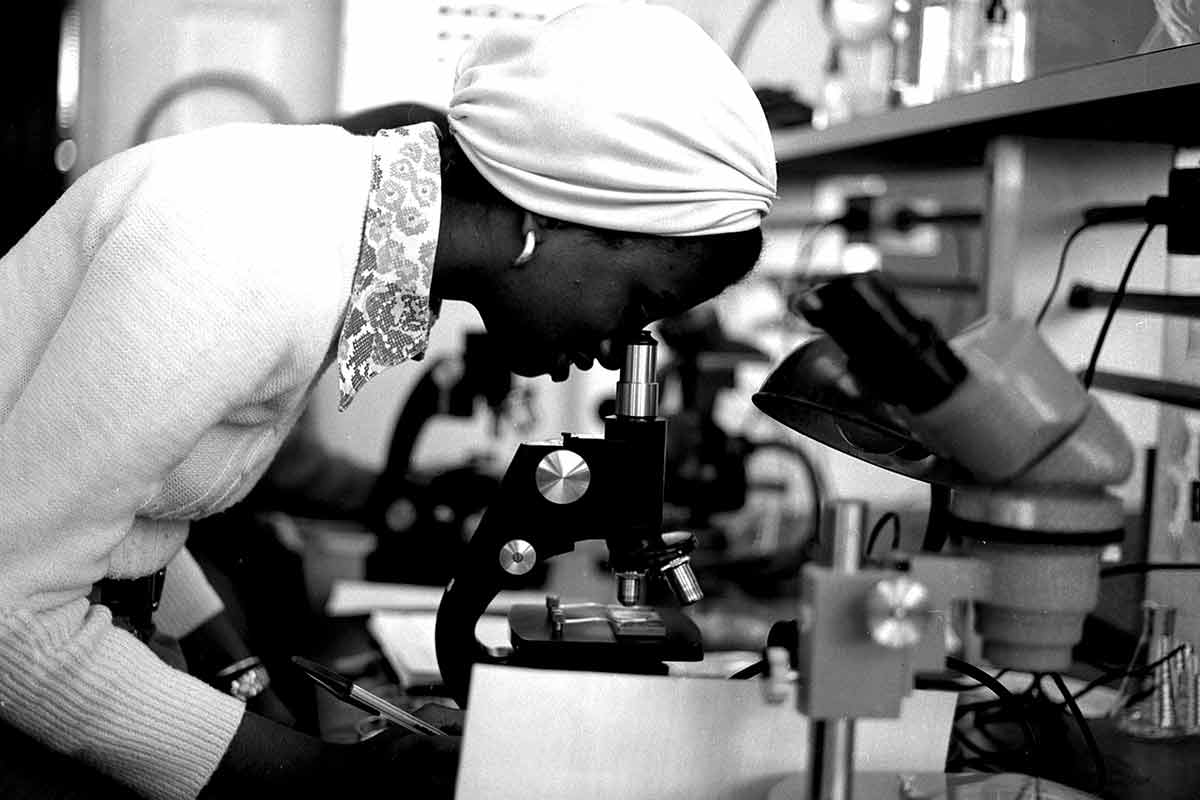 Black and white photo of a person looking into a microscope