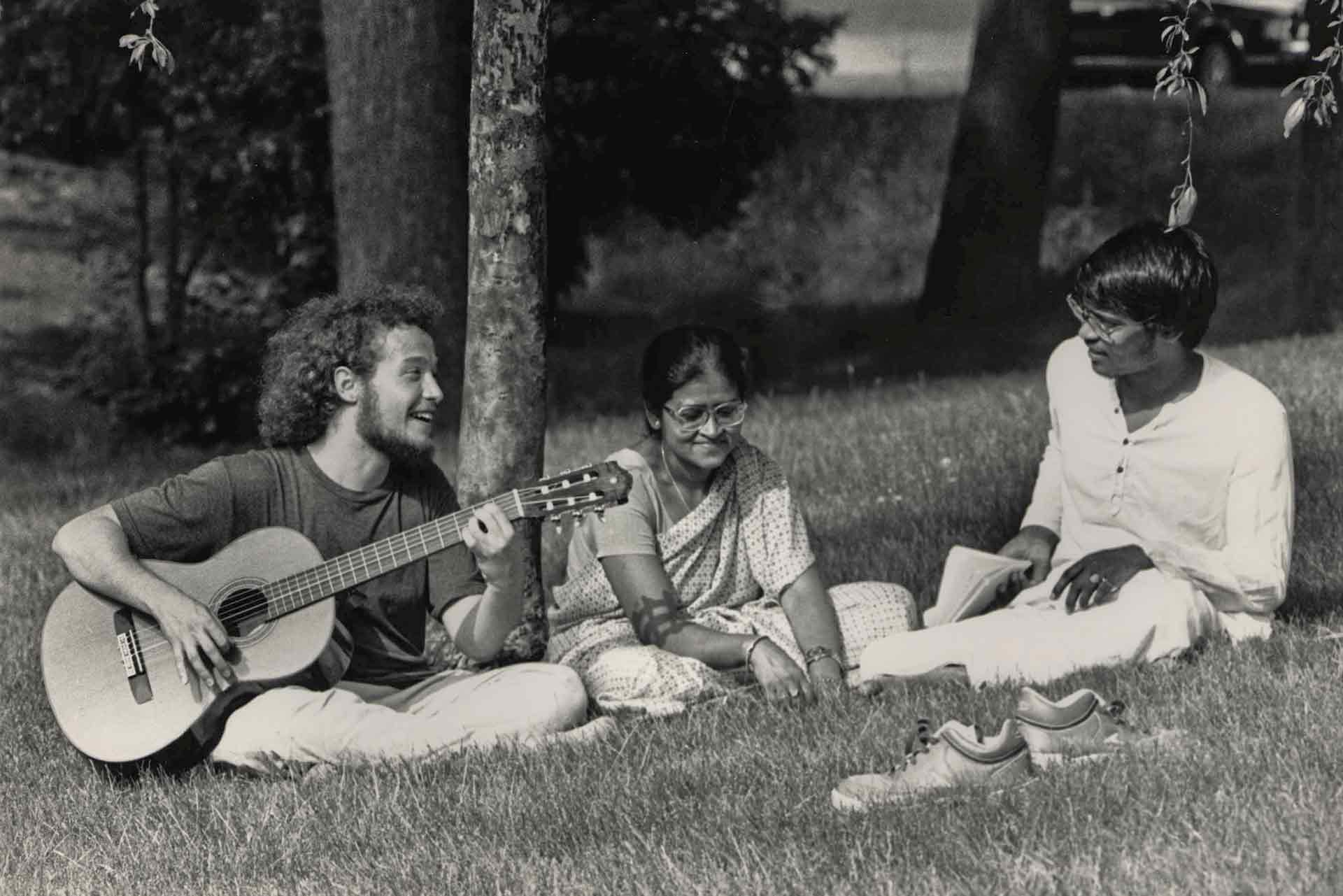 Black and white photo of people on campus, one with a guitar