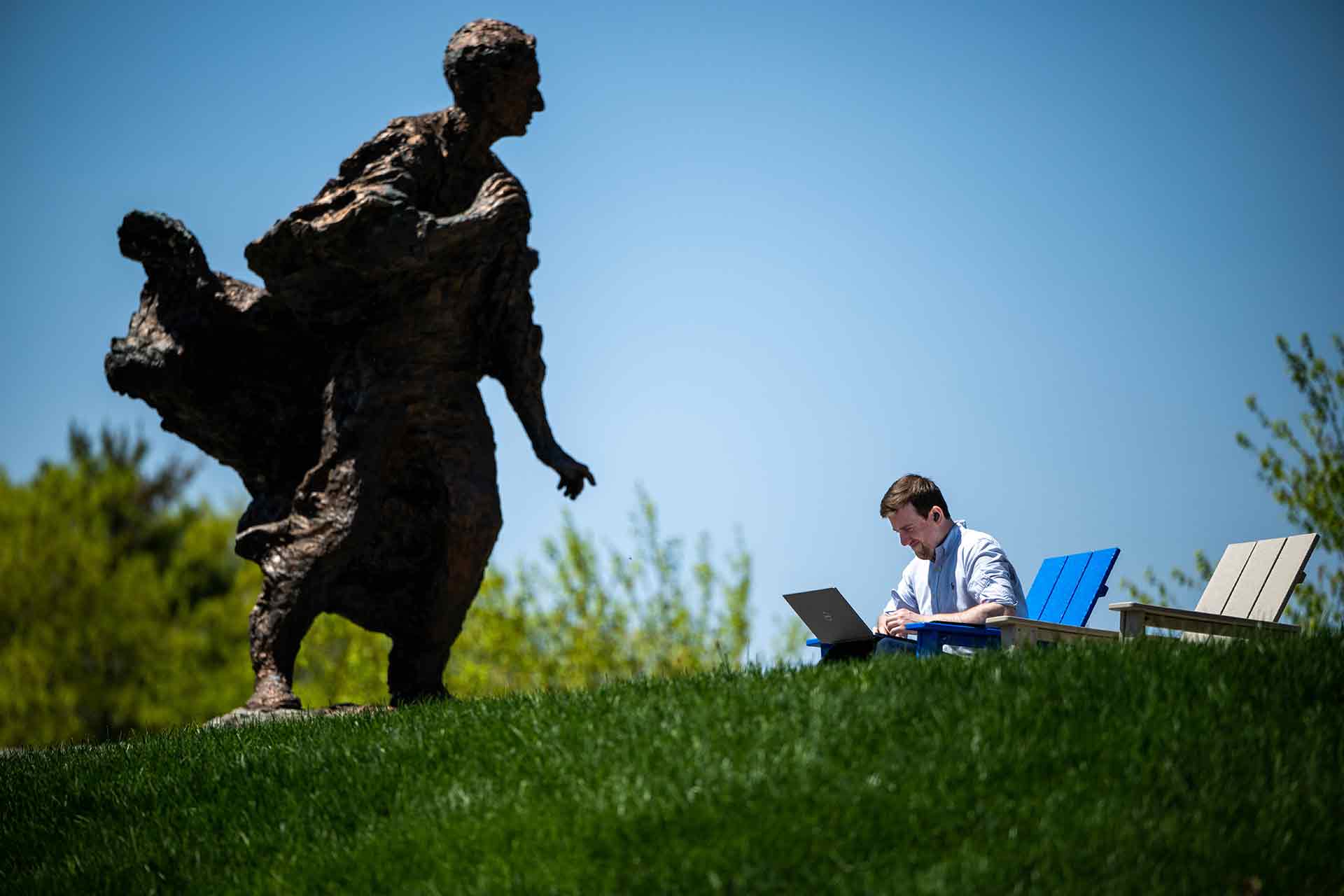 Color photo of a student on campus working on a laptop with the Louis Brandeis statue